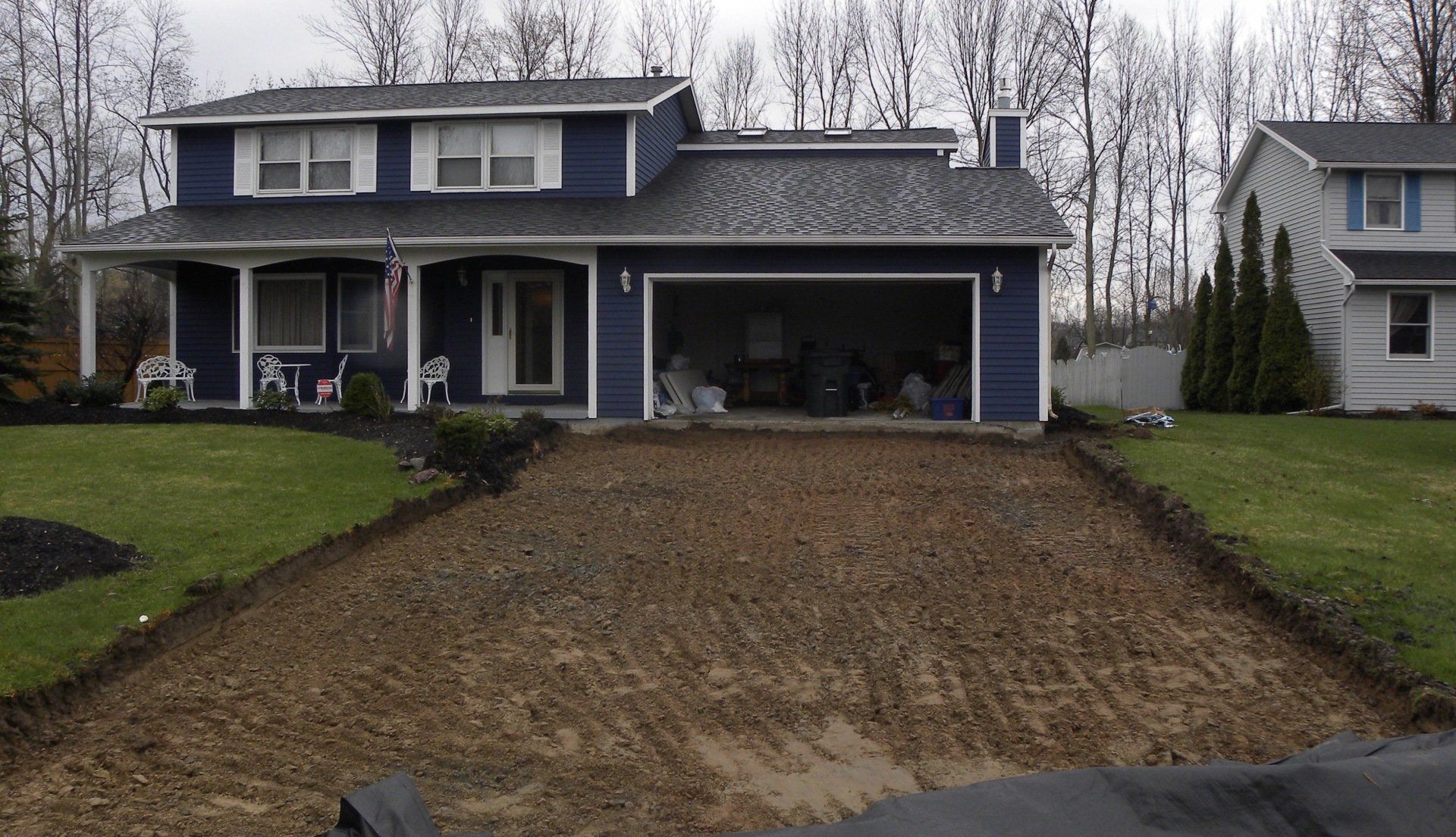 Driveway under construction in front of a blue two-story house.
