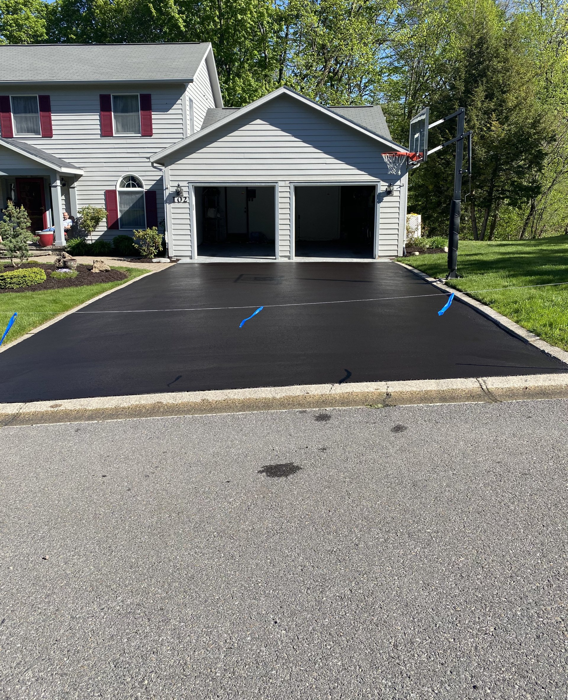Freshly paved black driveway in front of a gray house and garage.