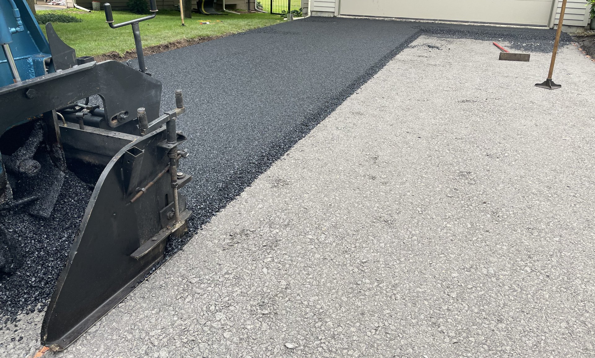 Asphalt paving machine laying blacktop on a driveway, next to a gravel edge.
